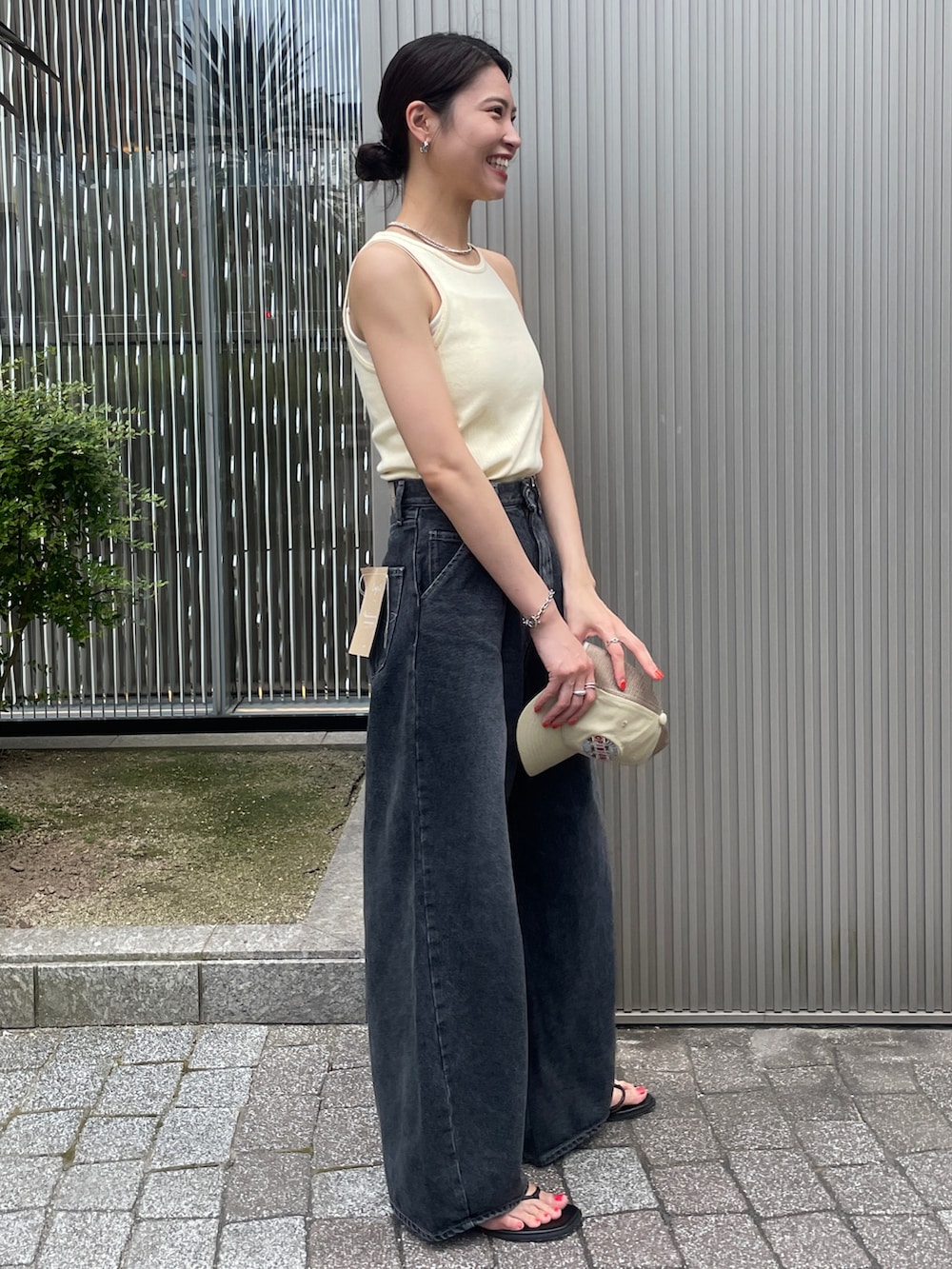 イエロー系のタンクトップ、ブラック系のデニムパンツ、ブラック系のサンダルを着用したレディースの夏コーディネートの2枚目の写真