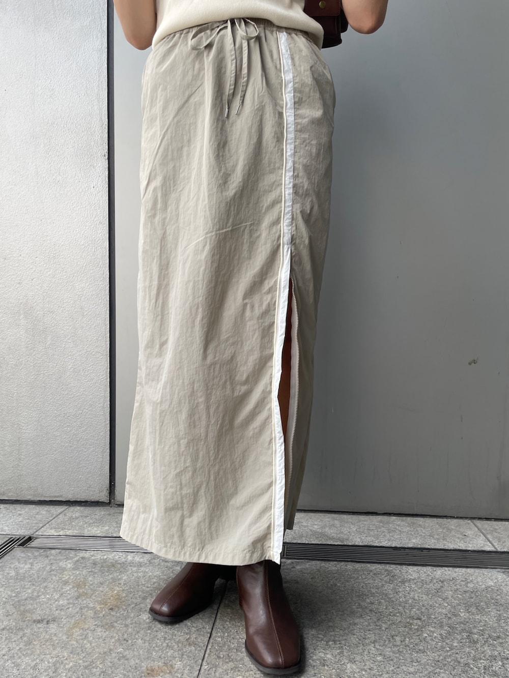 ベージュ系のスカート、ホワイト系のTシャツ/カットソー、ブラウン系のブーツを着用したレディースの夏コーディネートの5枚目の写真