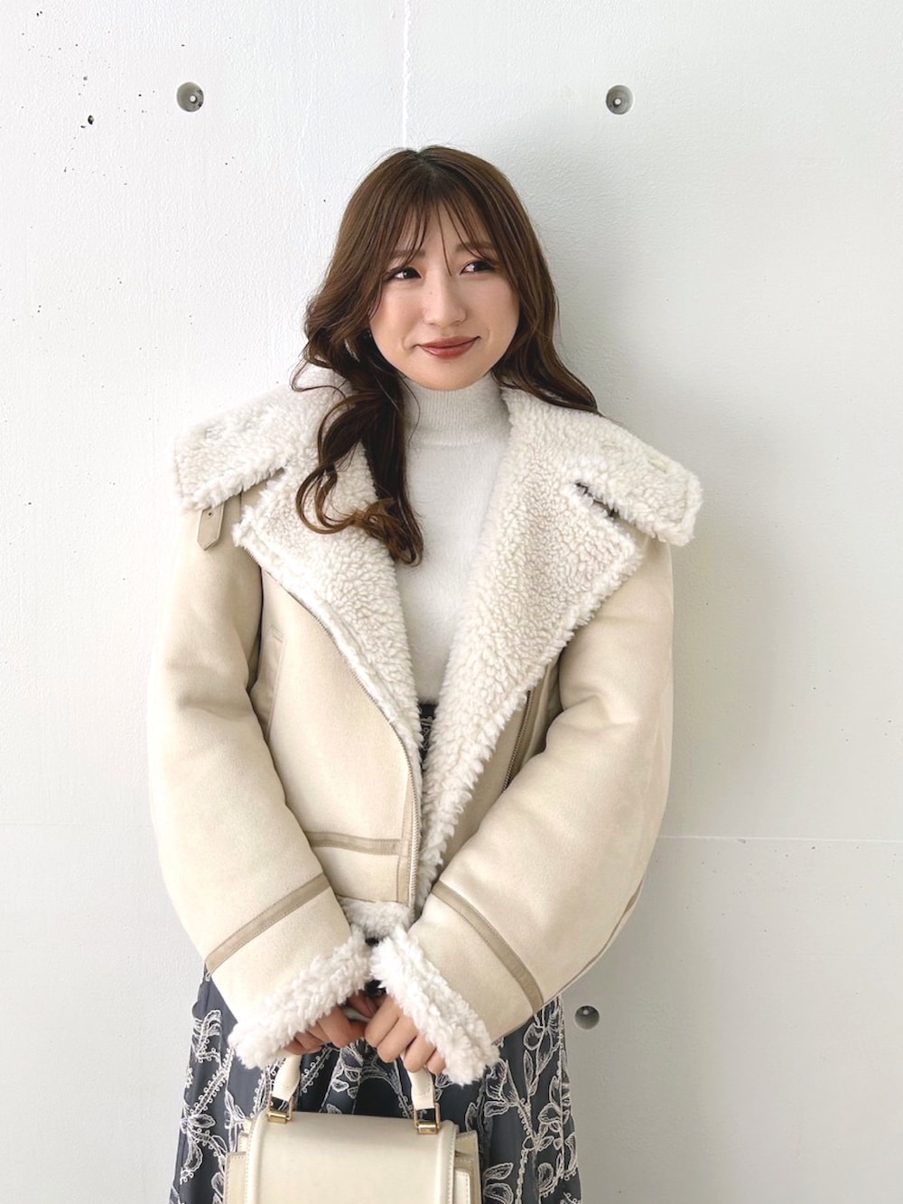 グレー系のスカート、ベージュ系のムートンコート、ホワイト系のニット/セーターを着用したレディースの秋コーディネートの2枚目の写真