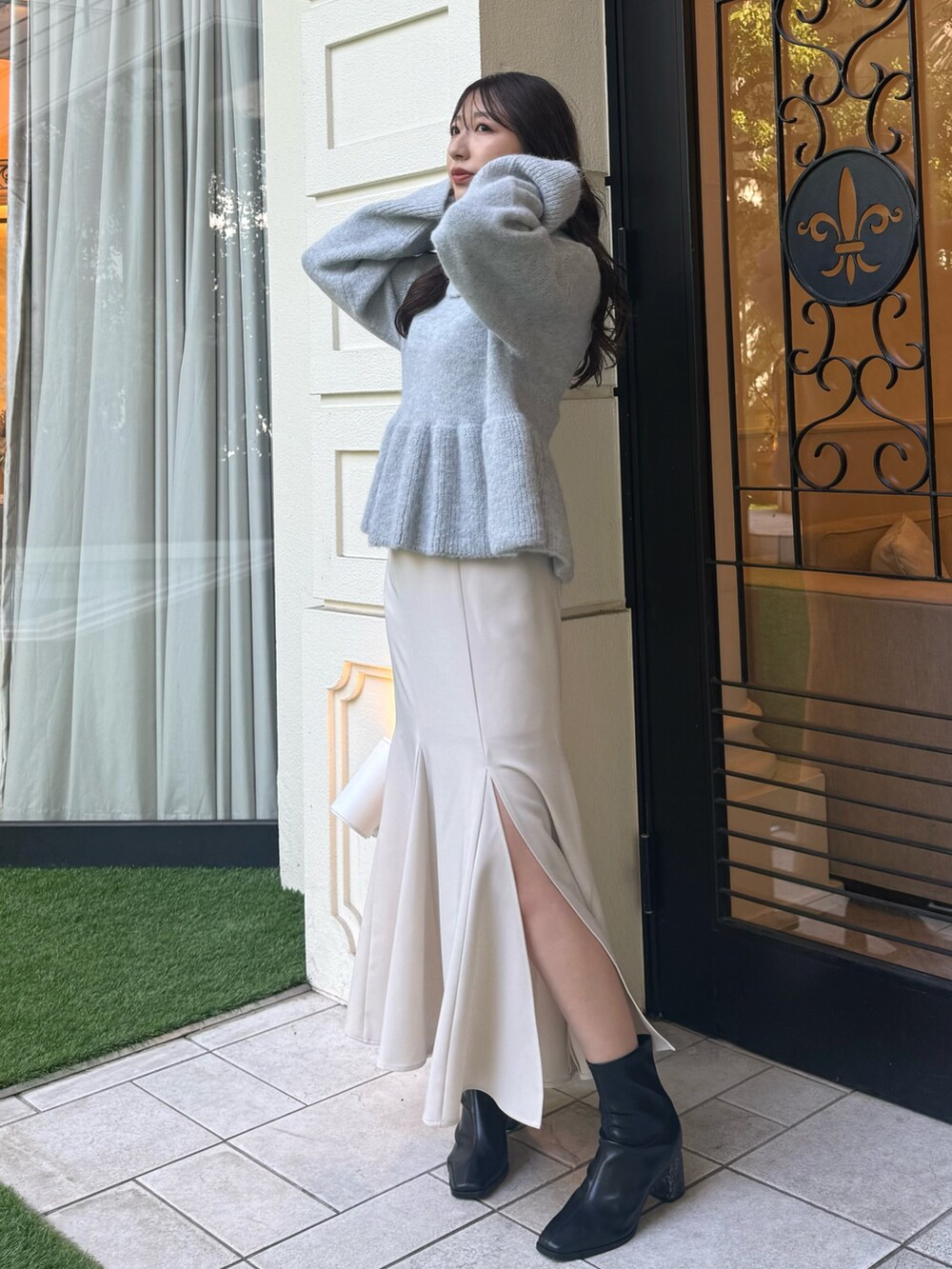 グレー系のニット/セーター、ホワイト系のスカート、ブラック系のブーツを着用したレディースの秋コーディネートの2枚目の写真