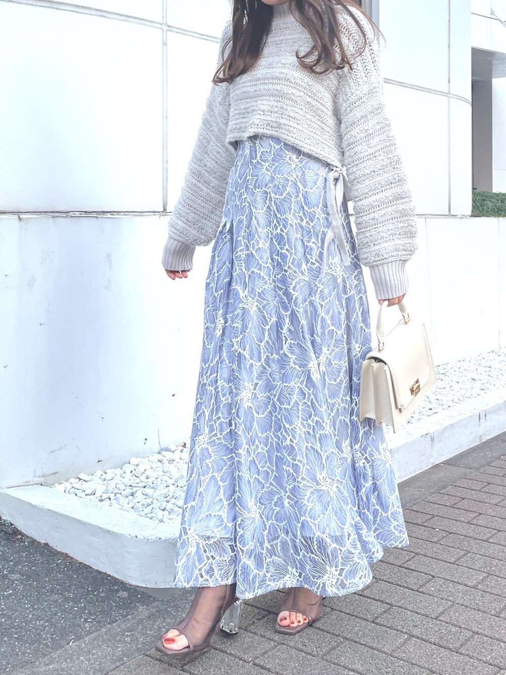 グレー系のニット/セーター、ブルー系のスカート、ホワイト系のハンドバッグを着用したレディースの冬コーディネートの2枚目の写真