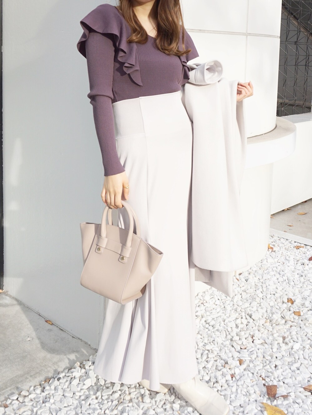 パープル系のニット/セーター、ホワイト系のスカート、ベージュ系のハンドバッグを着用したレディースの冬コーディネートの2枚目の写真