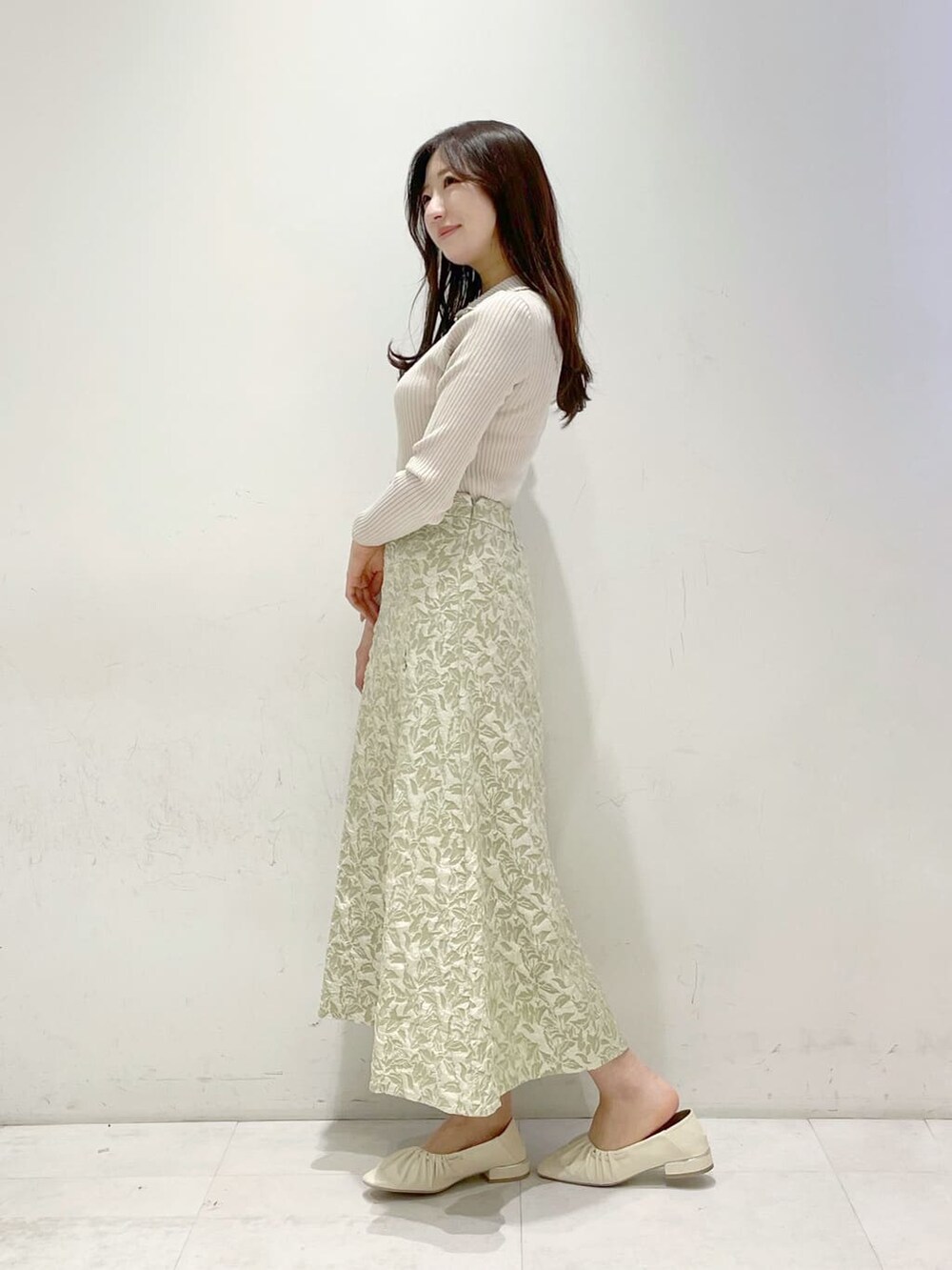 グリーン系のスカート、ホワイト系のパンプス、ベージュ系のニット/セーターを着用したレディースの冬コーディネートの2枚目の写真