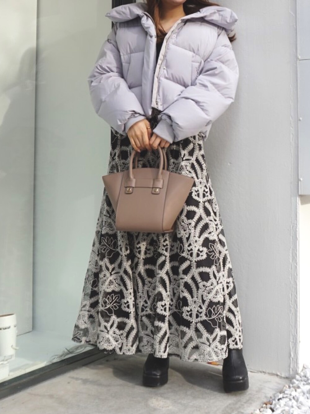 ブラック系のブーツ、ベージュ系のハンドバッグ、ブラック系のスカートを着用したレディースの冬コーディネートの2枚目の写真