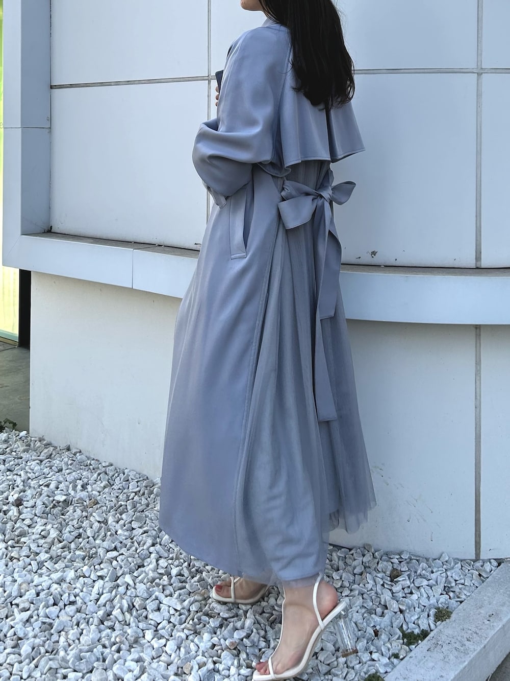 ブルー系のトレンチコート、ブラック系のワンピース、ホワイト系のブーツを着用したレディースの冬コーディネートの3枚目の写真