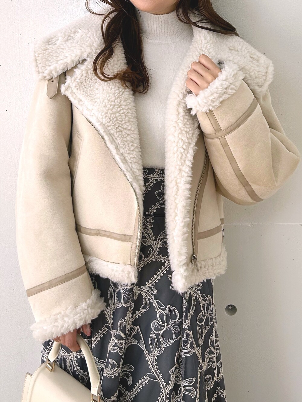 グレー系のスカート、ベージュ系のムートンコート、ホワイト系のニット/セーターを着用したレディースの秋コーディネートの3枚目の写真