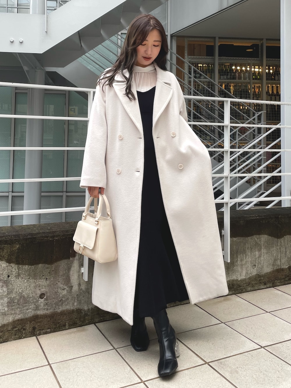ブラック系のワンピース、ホワイト系のハンドバッグ、ブラック系のブーツを着用したレディースの冬コーディネートの4枚目の写真