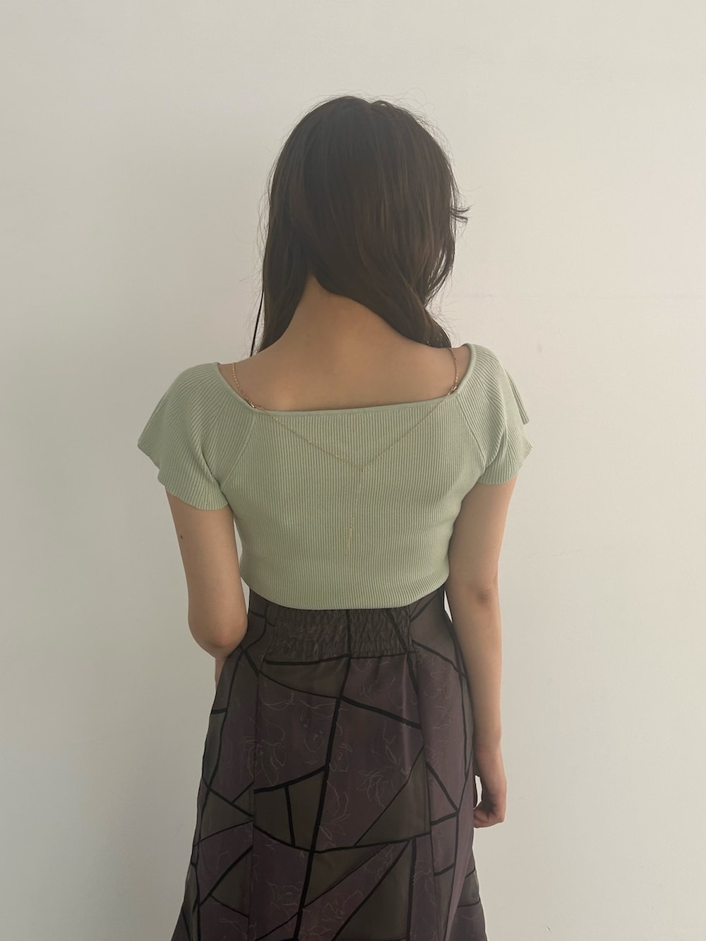 グリーン系のニット/セーター、ブラウン系のスカート、グレー系のパンプスを着用したレディースの夏コーディネートの2枚目の写真