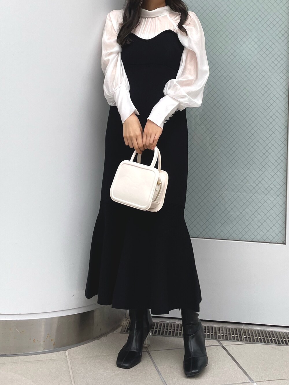 ブラック系のワンピース、ホワイト系のハンドバッグ、ブラック系のブーツを着用したレディースの冬コーディネートの2枚目の写真
