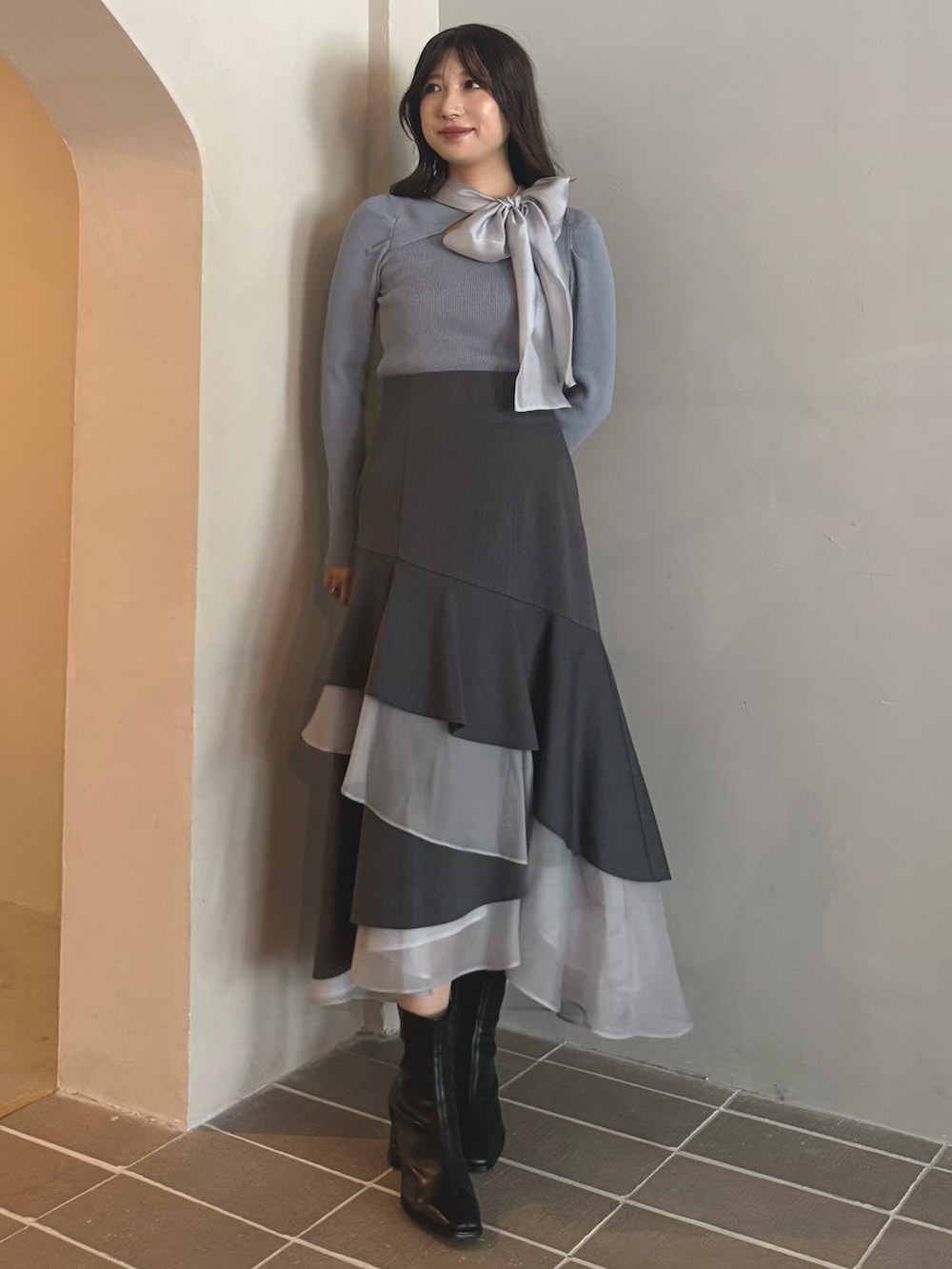 ブルー系のニット/セーター、グレー系のスカート、ブラック系のブーツを着用したレディースの秋コーディネートの2枚目の写真