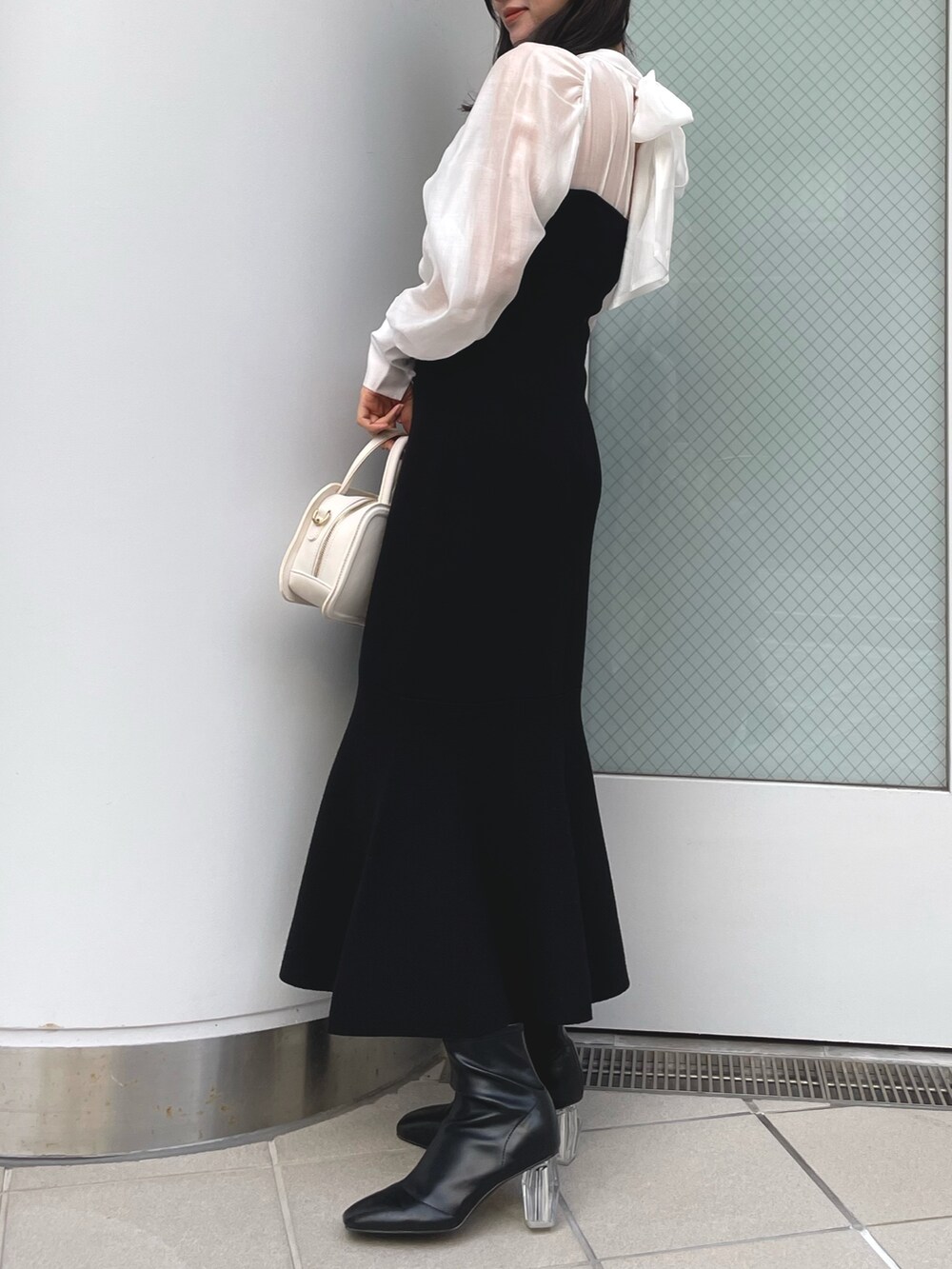 ブラック系のワンピース、ホワイト系のハンドバッグ、ブラック系のブーツを着用したレディースの冬コーディネートの3枚目の写真