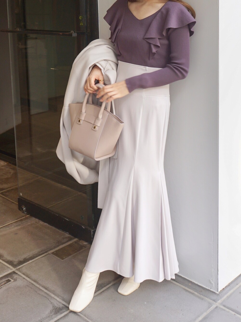 パープル系のニット/セーター、ホワイト系のスカート、ベージュ系のハンドバッグを着用したレディースの冬コーディネートの3枚目の写真