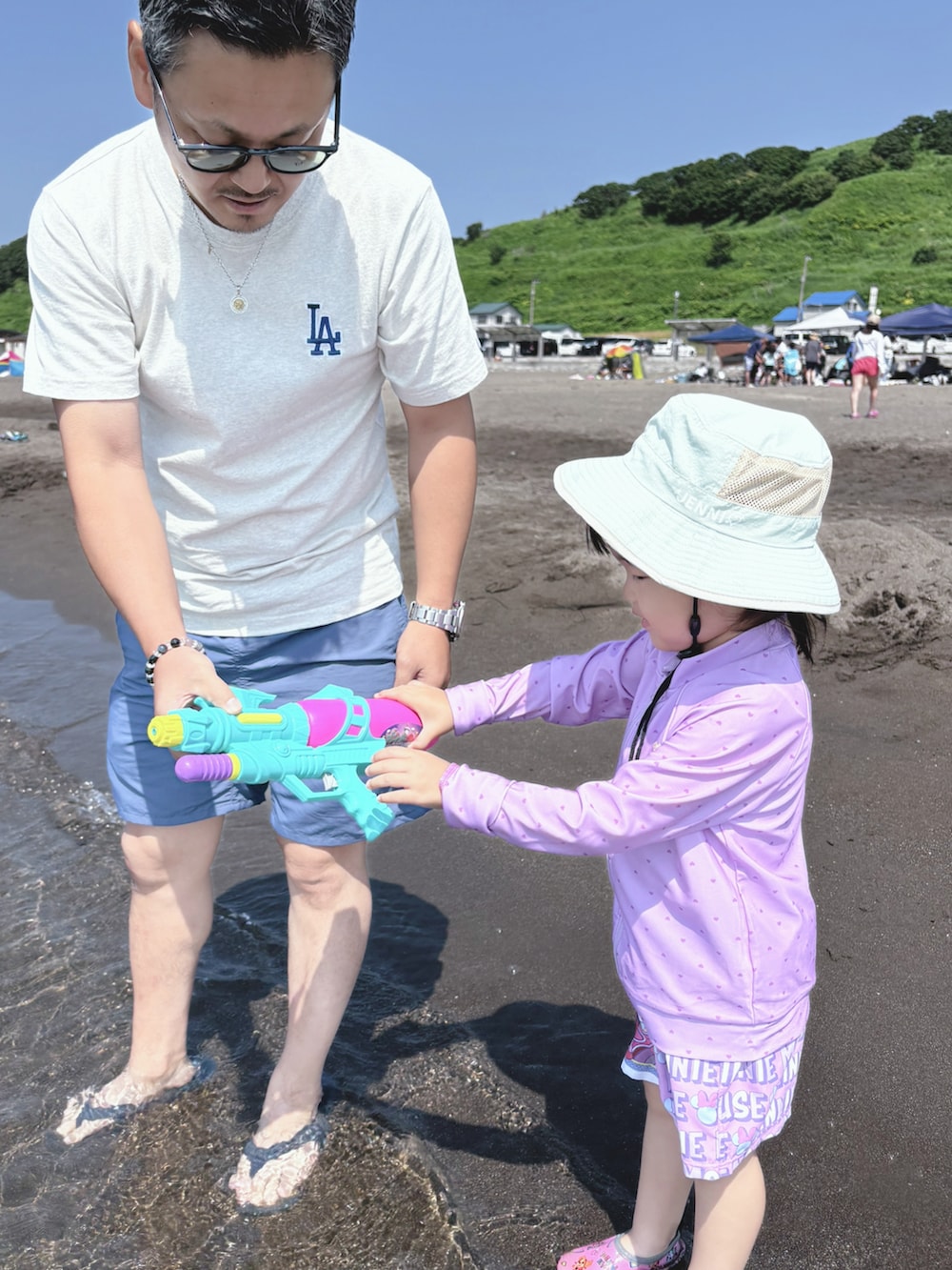 ピンク系の水着、パープル系のラッシュガード、グリーン系のハットを着用したキッズの夏コーディネートの4枚目の写真