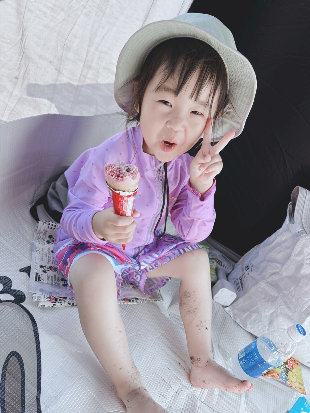 ピンク系の水着、パープル系のラッシュガード、グリーン系のハットを着用したキッズの夏コーディネートの3枚目の写真