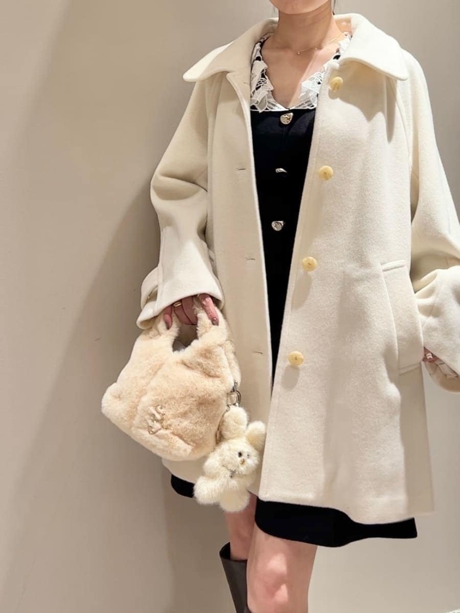 ホワイト系のステンカラーコート、イエロー系のハンドバッグ、ブラック系のワンピースを着用したレディースの冬コーディネートの4枚目の写真