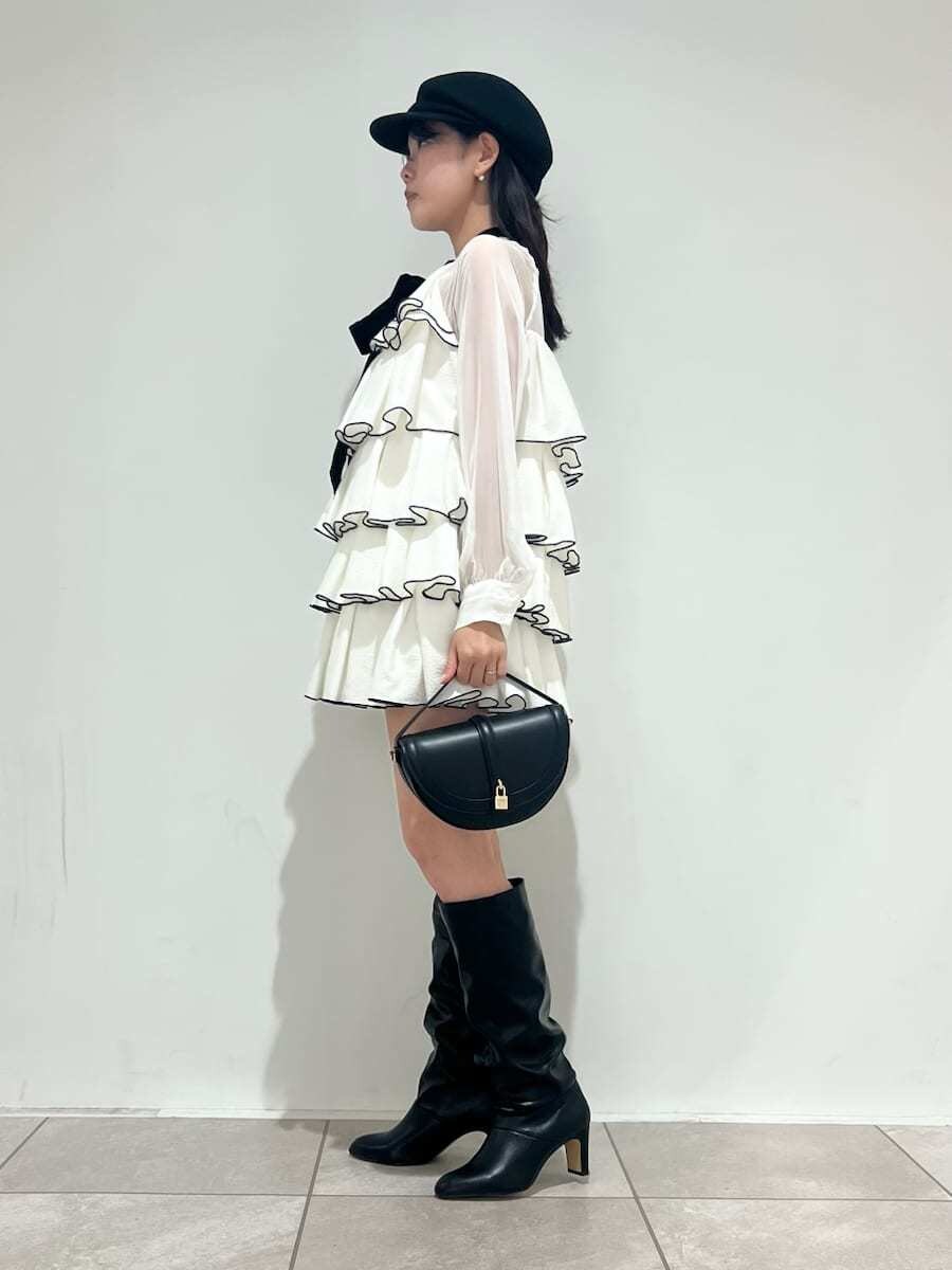 ブラック系のハンドバッグ、ホワイト系のドレス、ブラック系のブーツを着用したレディースの冬コーディネートの2枚目の写真