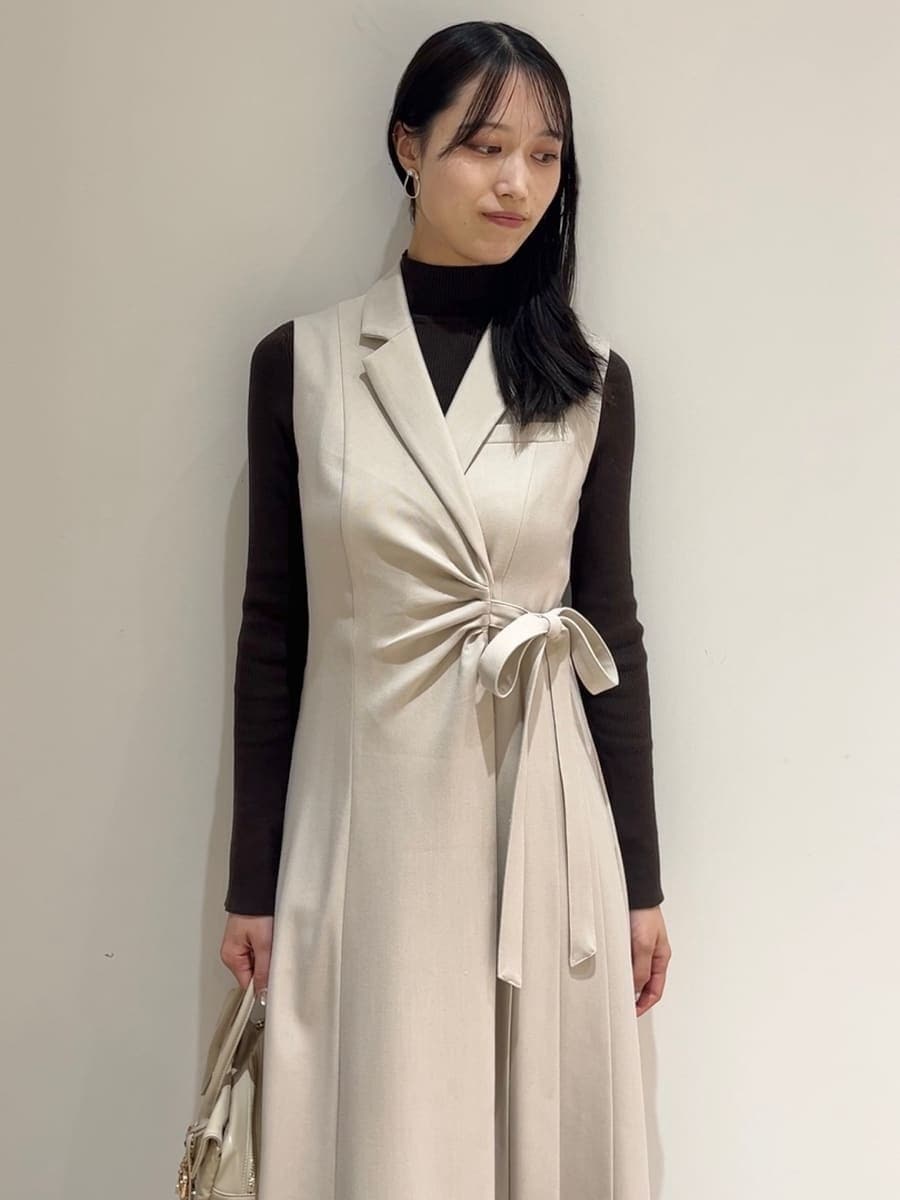 ブラウン系のステンカラーコート、ベージュ系のワンピース、ブラウン系のニット/セーターを着用したレディースの秋コーディネートの6枚目の写真