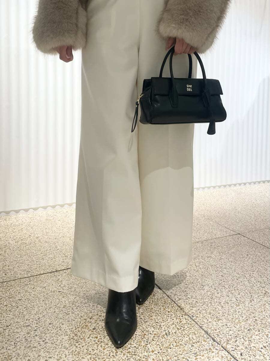 ベージュ系のチェスターコート、ブラック系のTシャツ/カットソー、ホワイト系のスラックスを着用したレディースの秋コーディネートの6枚目の写真