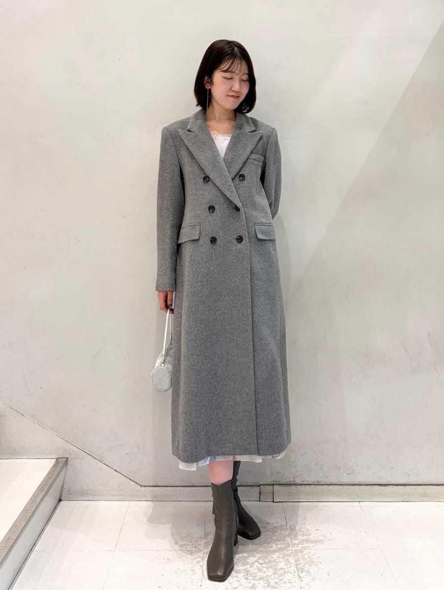 グレー系のワンピース、グレー系のチェスターコート、ゴールド系のイヤリングを着用したレディースの冬コーディネートの2枚目の写真