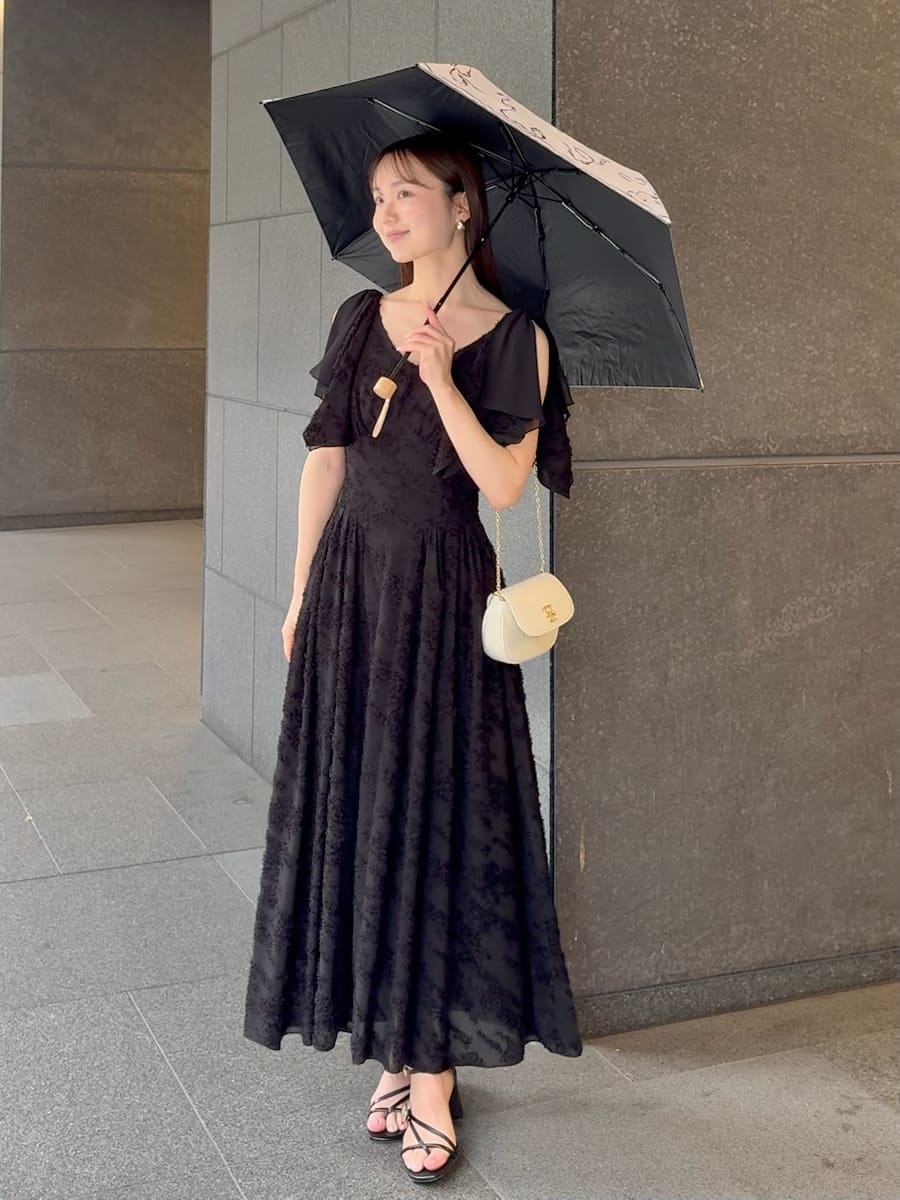 ブラック系のワンピース、ホワイト系のショルダーバッグ、ホワイト系の折りたたみ傘を着用したレディースの春コーディネートの2枚目の写真