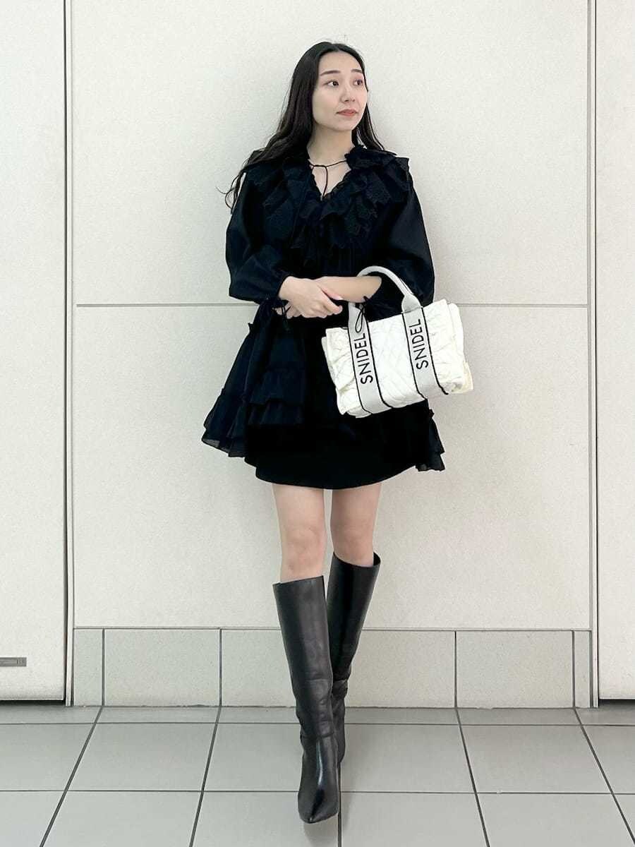 ブラック系のブーツ、ホワイト系のハンドバッグ、ブラック系のスカートを着用したレディースの冬コーディネートの2枚目の写真