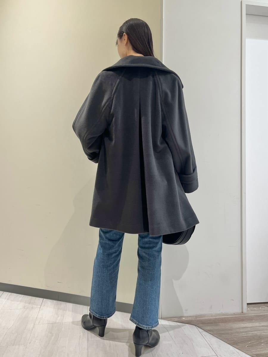 グレー系のステンカラーコート、レッド系のニット/セーター、ブルー系のデニムパンツを着用したレディースの秋コーディネートの3枚目の写真