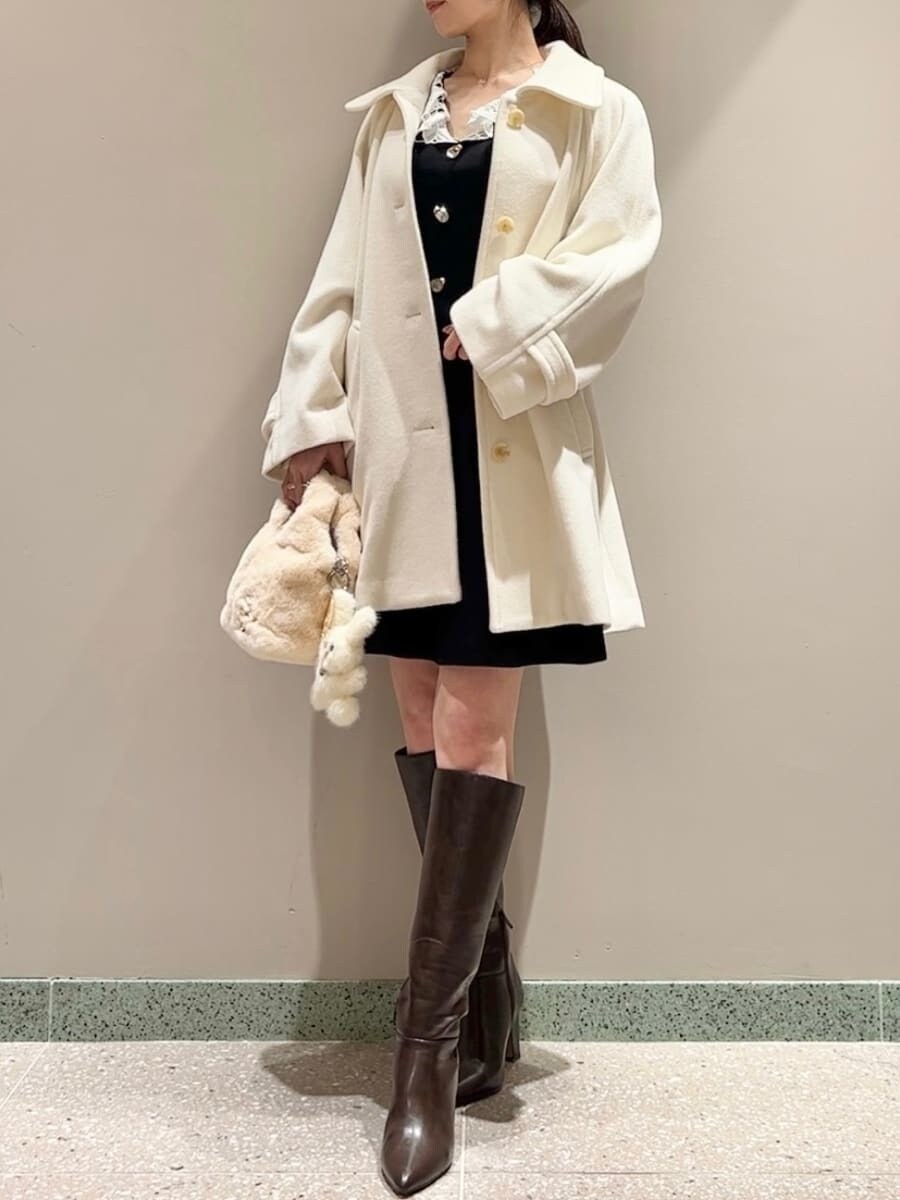 ホワイト系のステンカラーコート、イエロー系のハンドバッグ、ブラック系のワンピースを着用したレディースの冬コーディネートの2枚目の写真