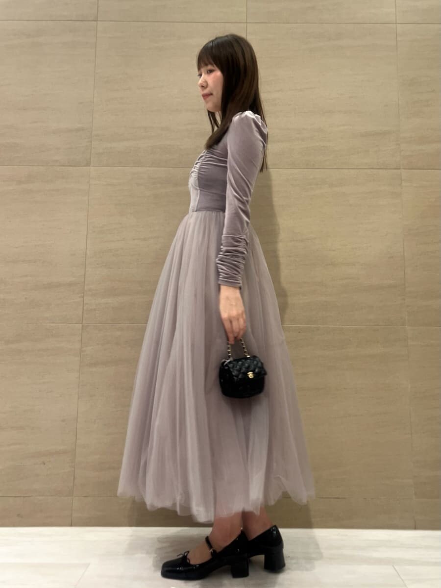 パープル系のワンピース、ブラック系のパンプス、ブラック系のショルダーバッグを着用したレディースの秋コーディネートの2枚目の写真