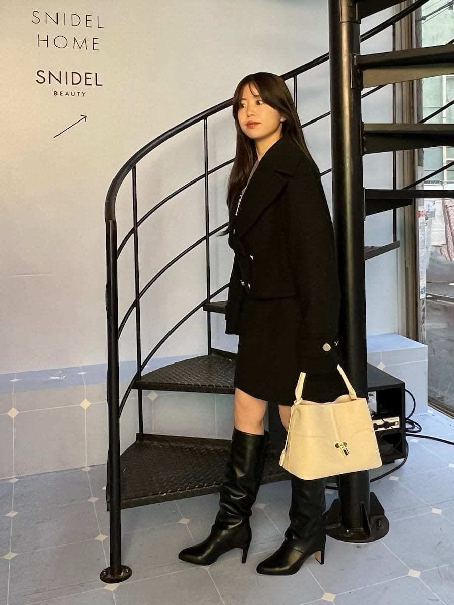 ブラック系のピーコート、ブラック系のスカート、ホワイト系のニット/セーターを着用したレディースの冬コーディネートの4枚目の写真