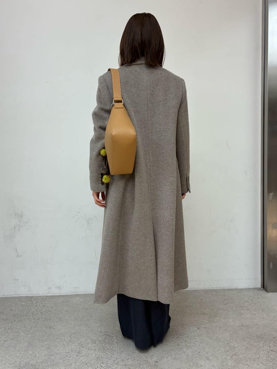 イエロー系のトートバッグ、グレー系のチェスターコート、ブルー系のその他パンツを着用したレディースの冬コーディネートの2枚目の写真