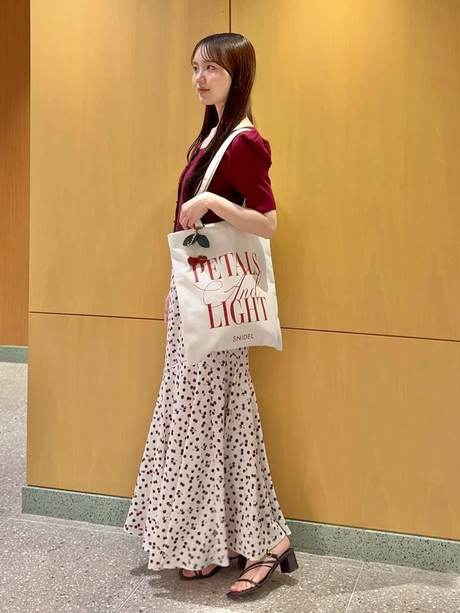 ホワイト系のトートバッグ、ホワイト系のスカート、レッド系のカーディガン/ボレロを着用したレディースの春コーディネートの2枚目の写真