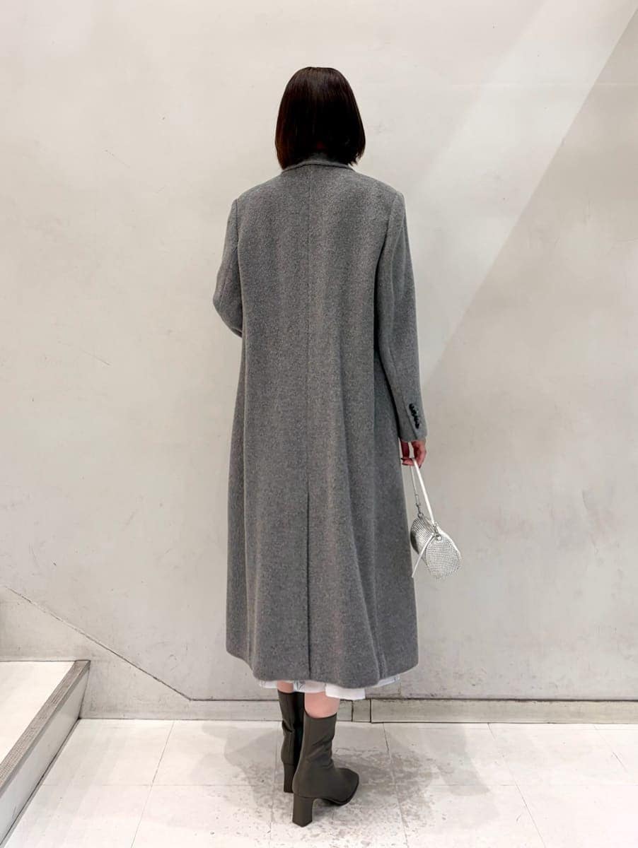 グレー系のワンピース、グレー系のチェスターコート、ゴールド系のイヤリングを着用したレディースの冬コーディネートの4枚目の写真