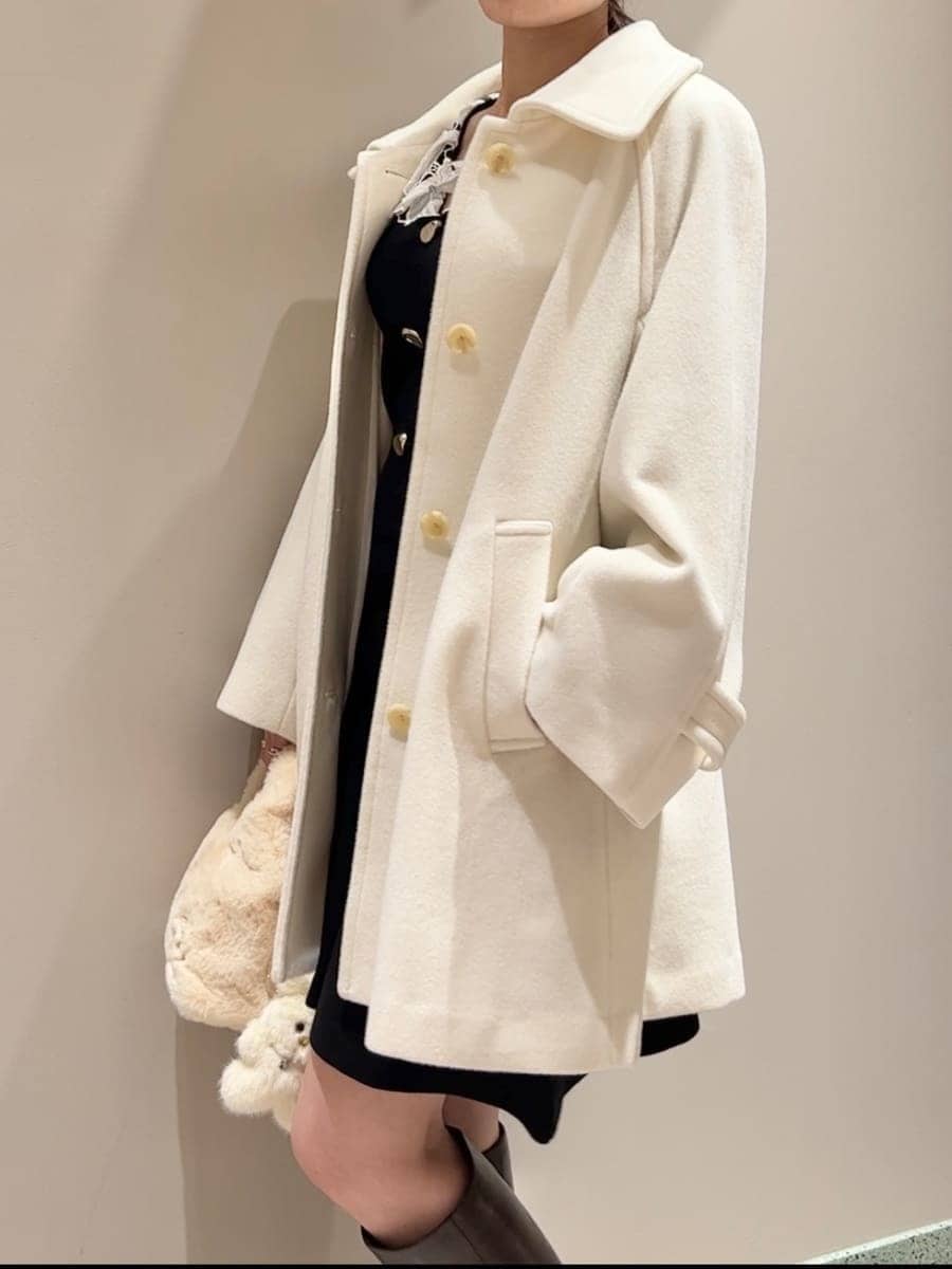 ホワイト系のステンカラーコート、イエロー系のハンドバッグ、ブラック系のワンピースを着用したレディースの冬コーディネートの5枚目の写真