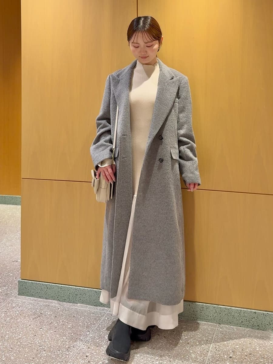 グレー系のチェスターコート、ホワイト系のワンピース、ブラック系のブーツを着用したレディースの冬コーディネートの2枚目の写真