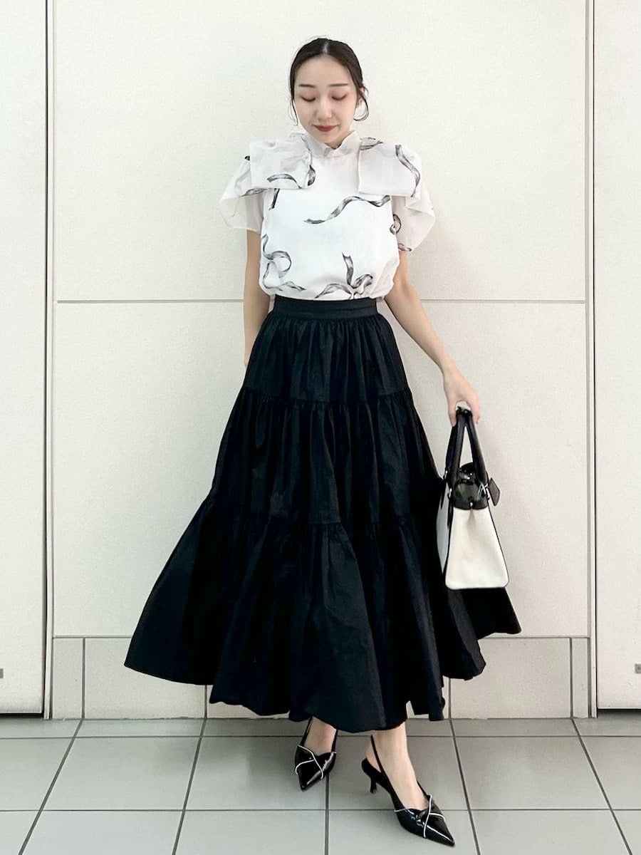 ブラック系のスカート、ブラック系のパンプス、ホワイト系のハンドバッグを着用したレディースの春コーディネートの2枚目の写真