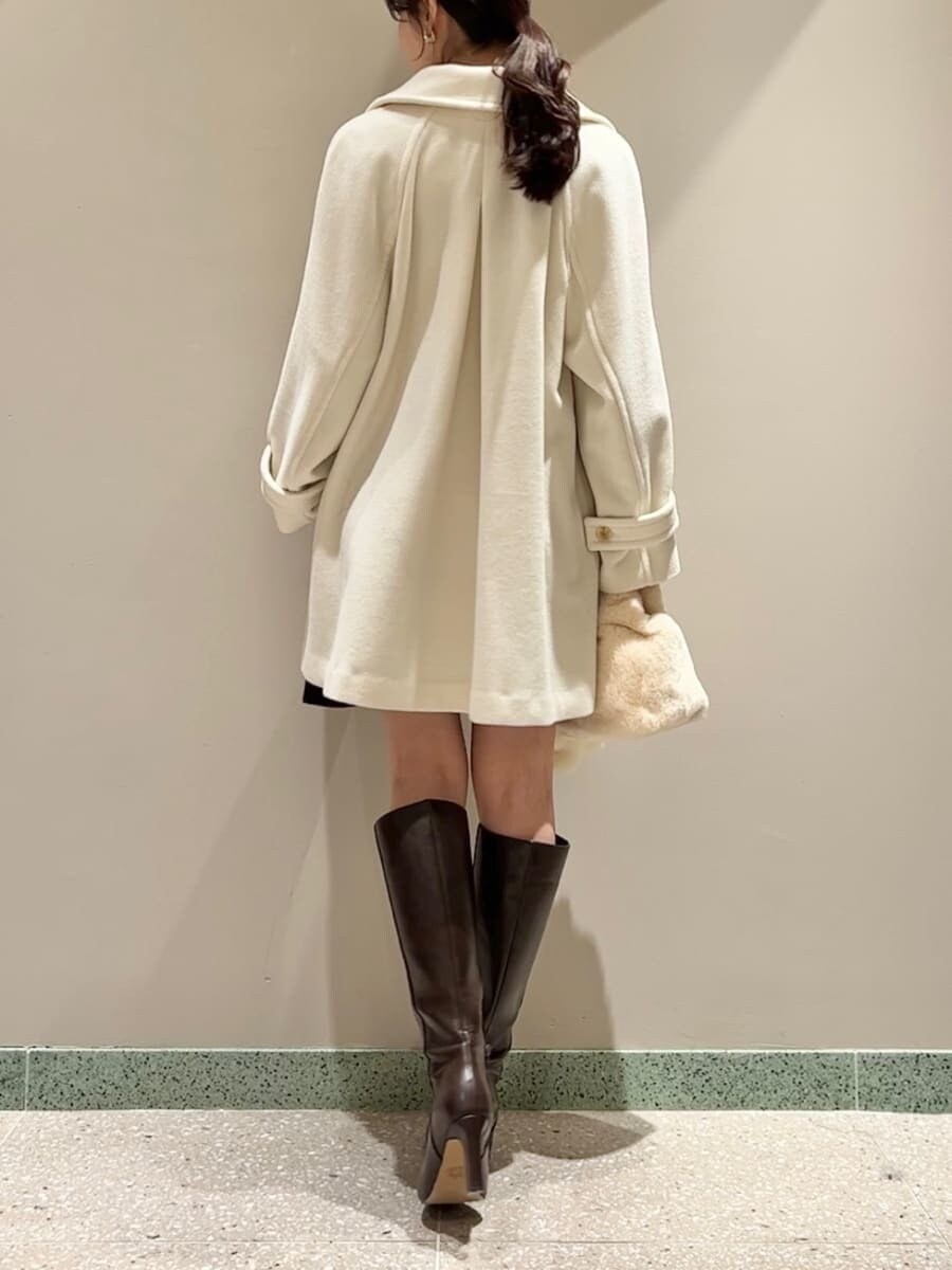 ホワイト系のステンカラーコート、イエロー系のハンドバッグ、ブラック系のワンピースを着用したレディースの冬コーディネートの3枚目の写真