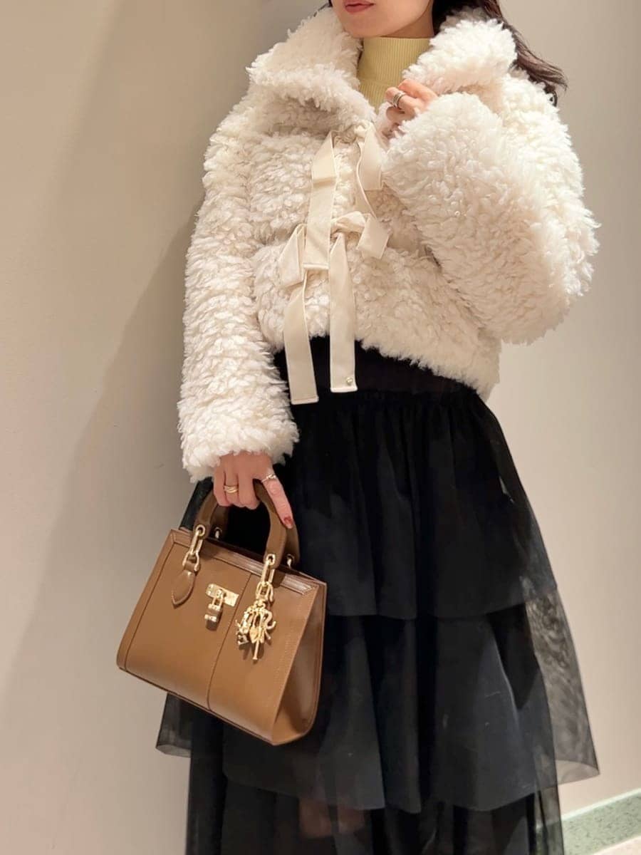 イエロー系のニット/セーター、ホワイト系のムートンコート、ブラック系のスカートを着用したレディースの秋コーディネートの4枚目の写真