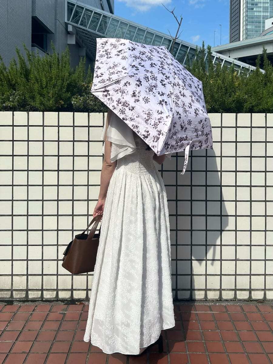 ホワイト系のワンピース、ブラウン系のハンドバッグ、ピンク系の折りたたみ傘を着用したレディースの春コーディネートの2枚目の写真