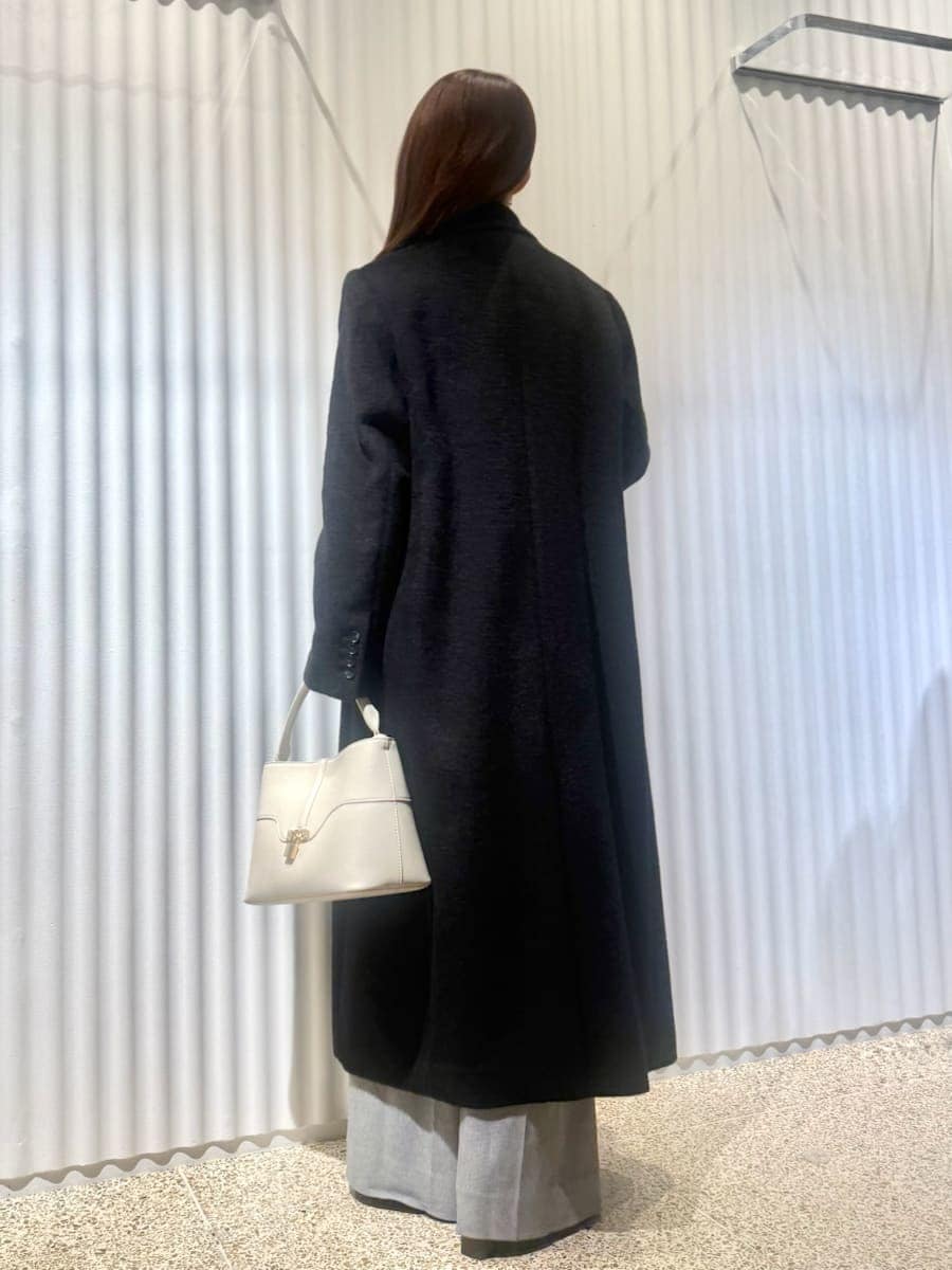 ブラック系のチェスターコート、ブルー系のニット/セーター、ホワイト系のハンドバッグを着用したレディースの冬コーディネートの2枚目の写真