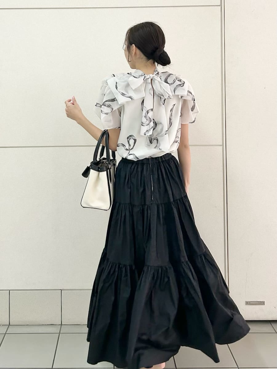 ブラック系のスカート、ブラック系のパンプス、ホワイト系のハンドバッグを着用したレディースの春コーディネートの4枚目の写真