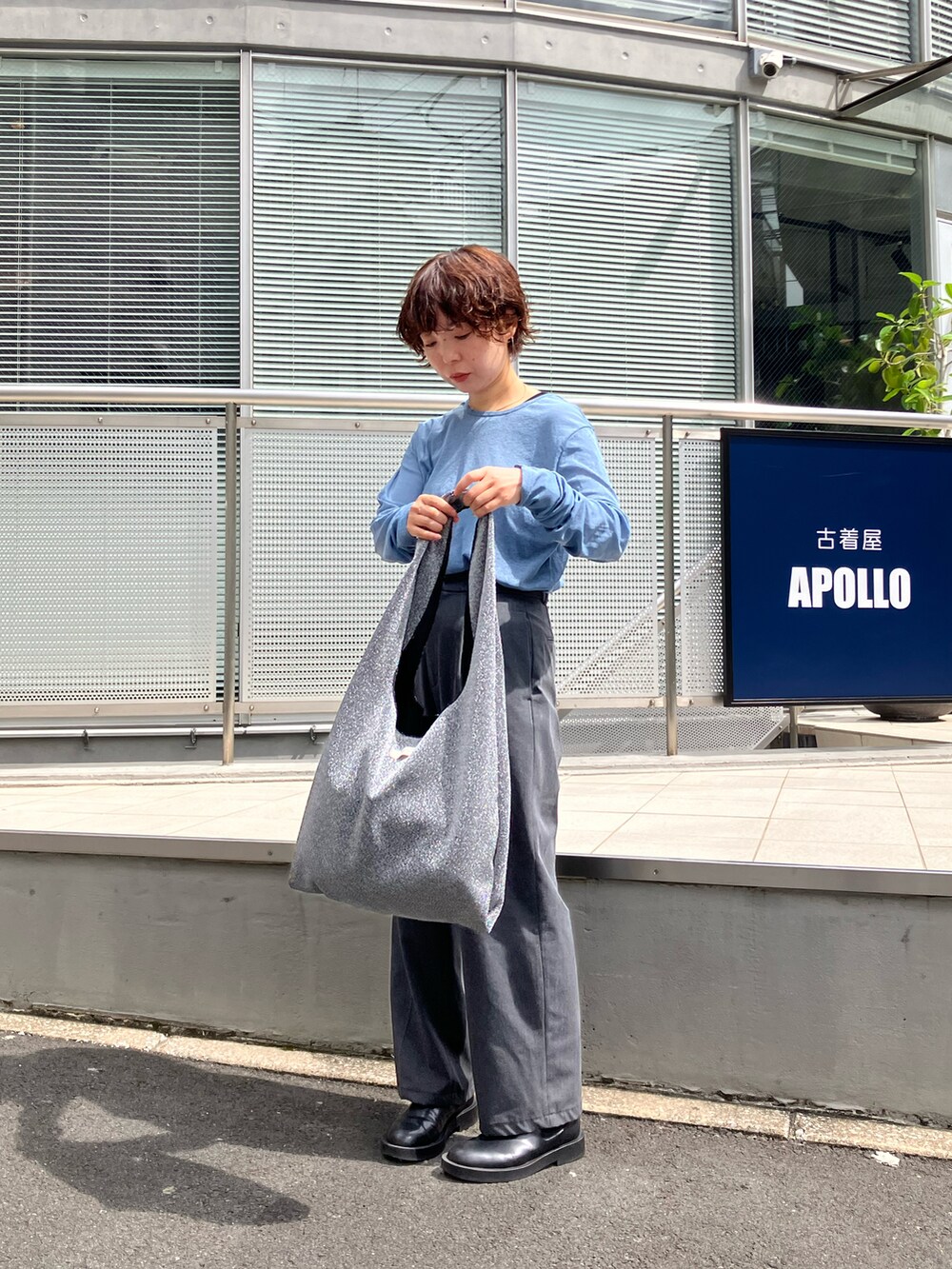 シルバー系のトートバッグ、ブラック系のブーツ、グレー系のパンツを着用したレディースの秋コーディネートの2枚目の写真