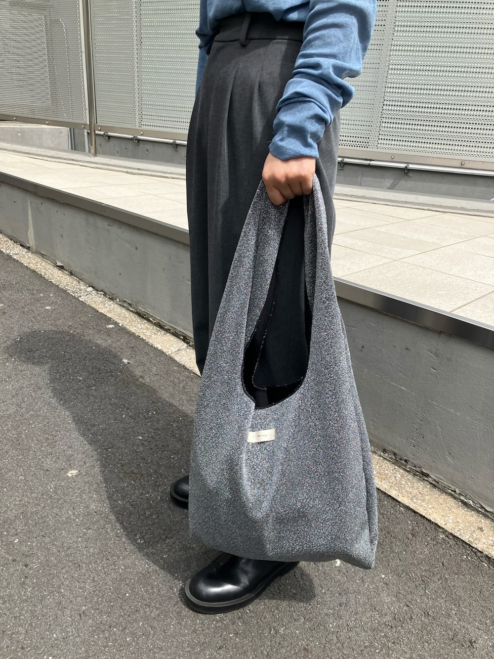 シルバー系のトートバッグ、ブラック系のブーツ、グレー系のパンツを着用したレディースの秋コーディネートの3枚目の写真