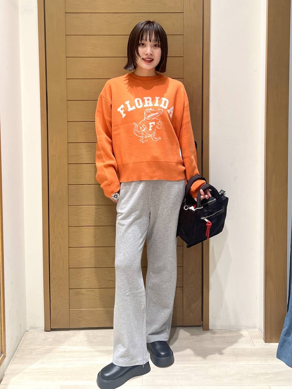 ブラック系のショルダーバッグ、オレンジ系のニット/セーター、グレー系のその他パンツを着用したレディースの秋コーディネートの2枚目の写真