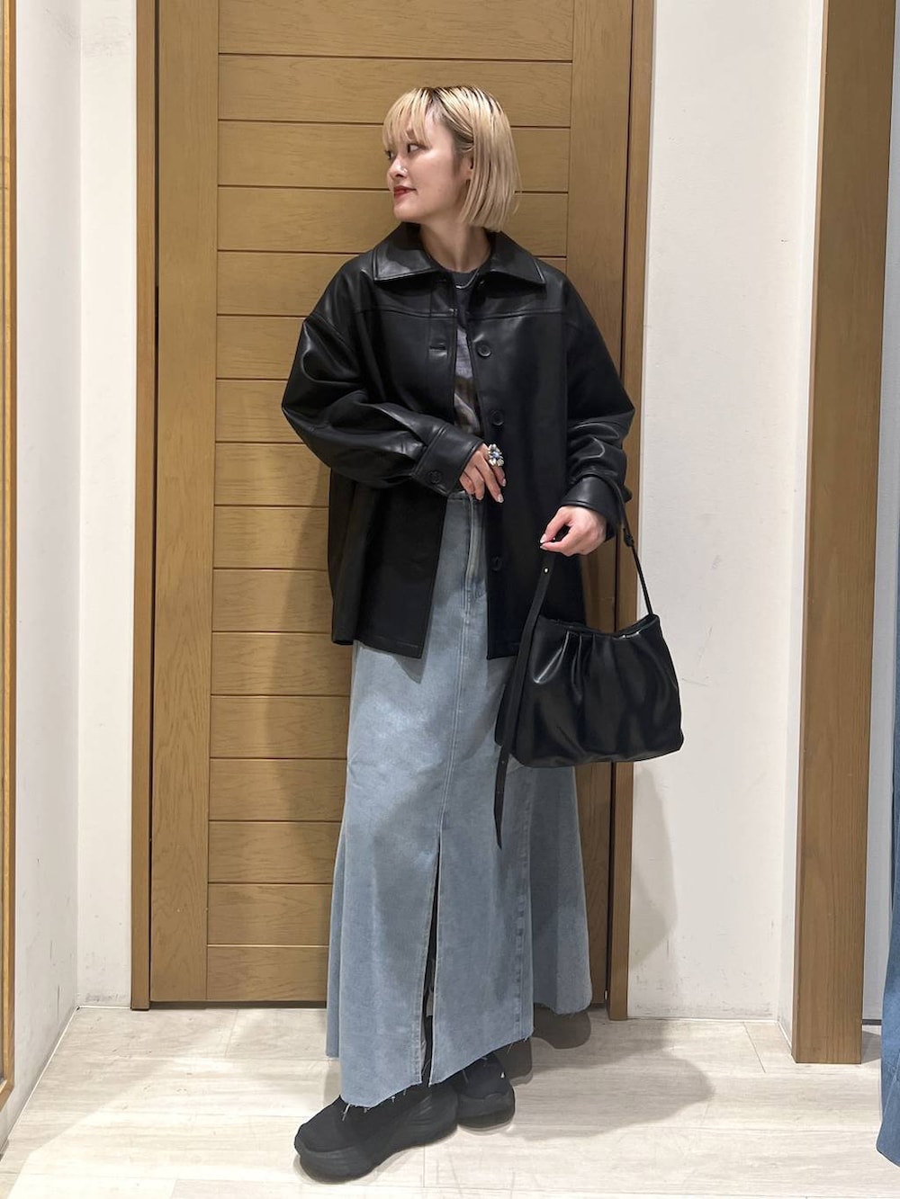 ブラック系のハンドバッグ、ブラック系のブルゾン、ブルー系のスカートを着用したレディースの秋コーディネートの3枚目の写真