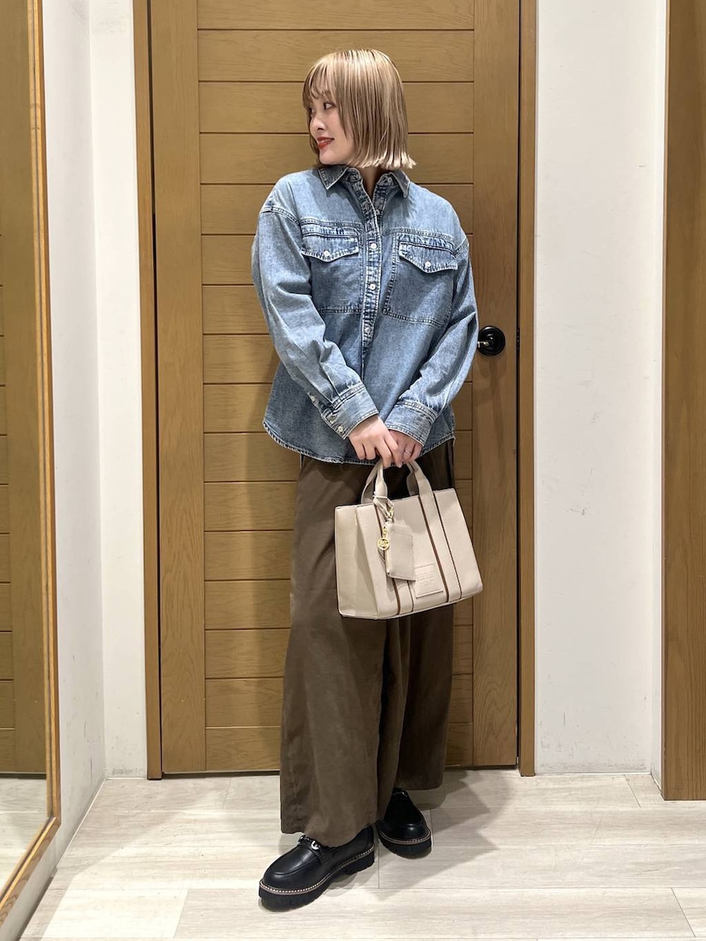 ブラック系のローファー、ベージュ系のハンドバッグ、ブルー系のシャツ/ブラウスを着用したレディースの春コーディネートの2枚目の写真
