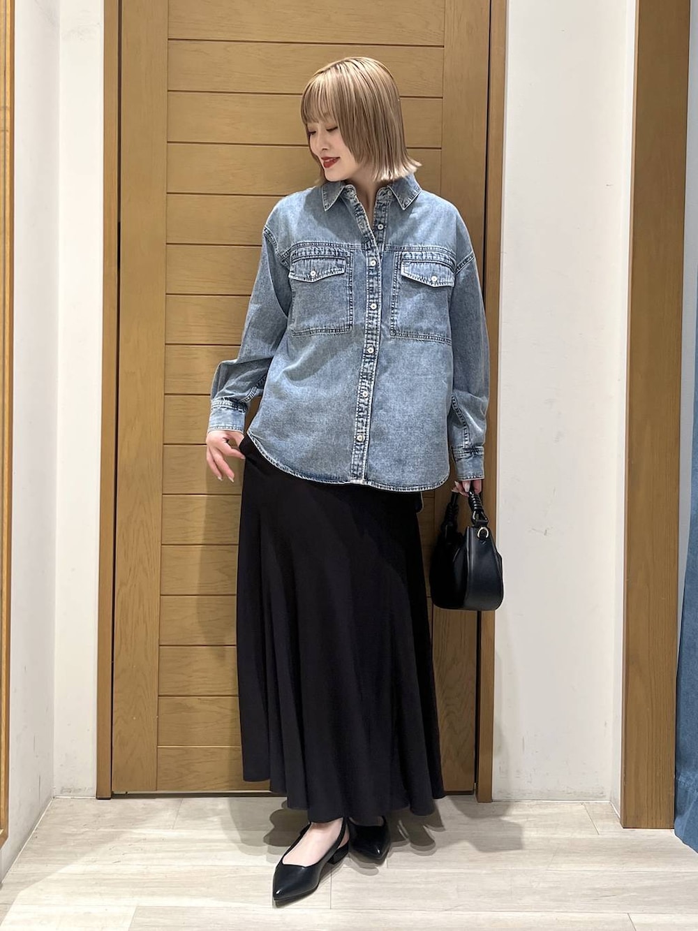 ブラック系のハンドバッグ、ブラック系のパンプス、ブルー系のシャツ/ブラウスを着用したレディースの春コーディネートの2枚目の写真