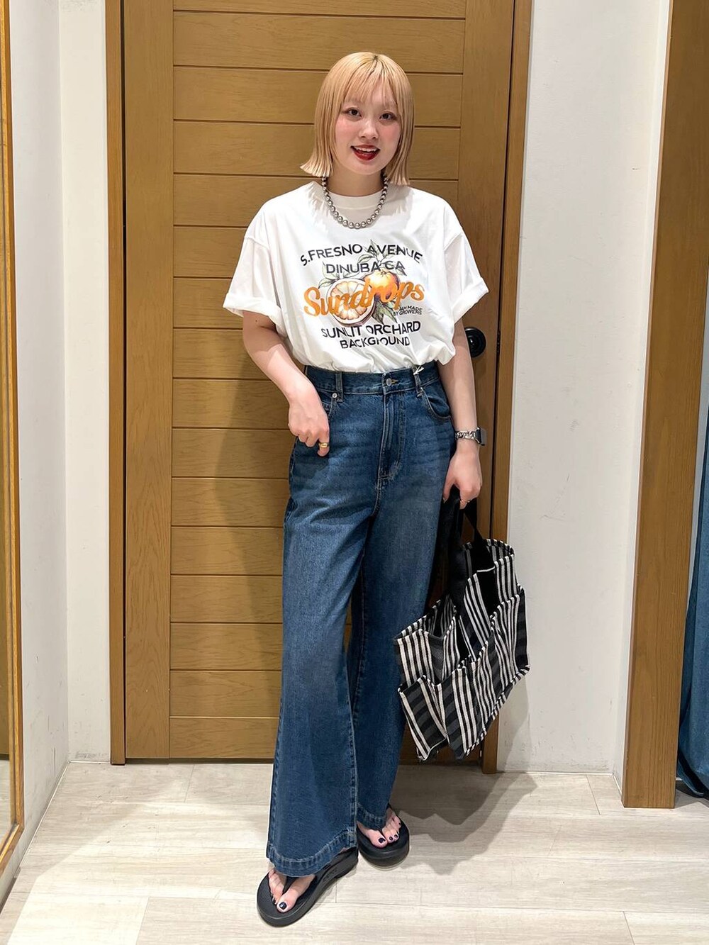 ブルー系のデニムパンツ、オレンジ系のTシャツ/カットソー、ブラック系のサンダルを着用したレディースの夏コーディネートの3枚目の写真