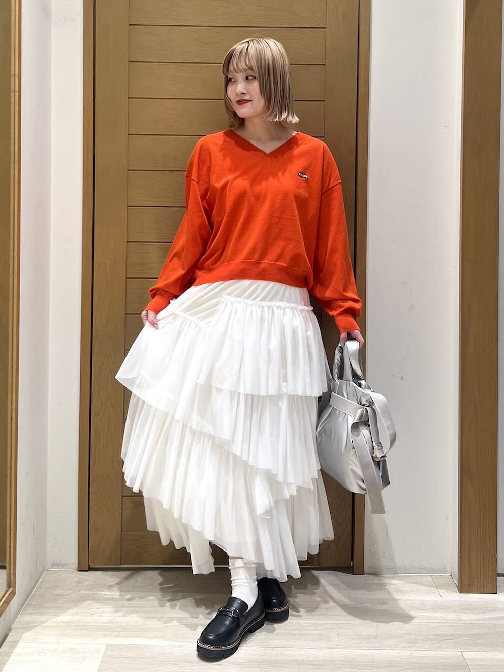 シルバー系のトートバッグ、ブラック系のローファー、オレンジ系のニット/セーターを着用したレディースの春コーディネートの2枚目の写真