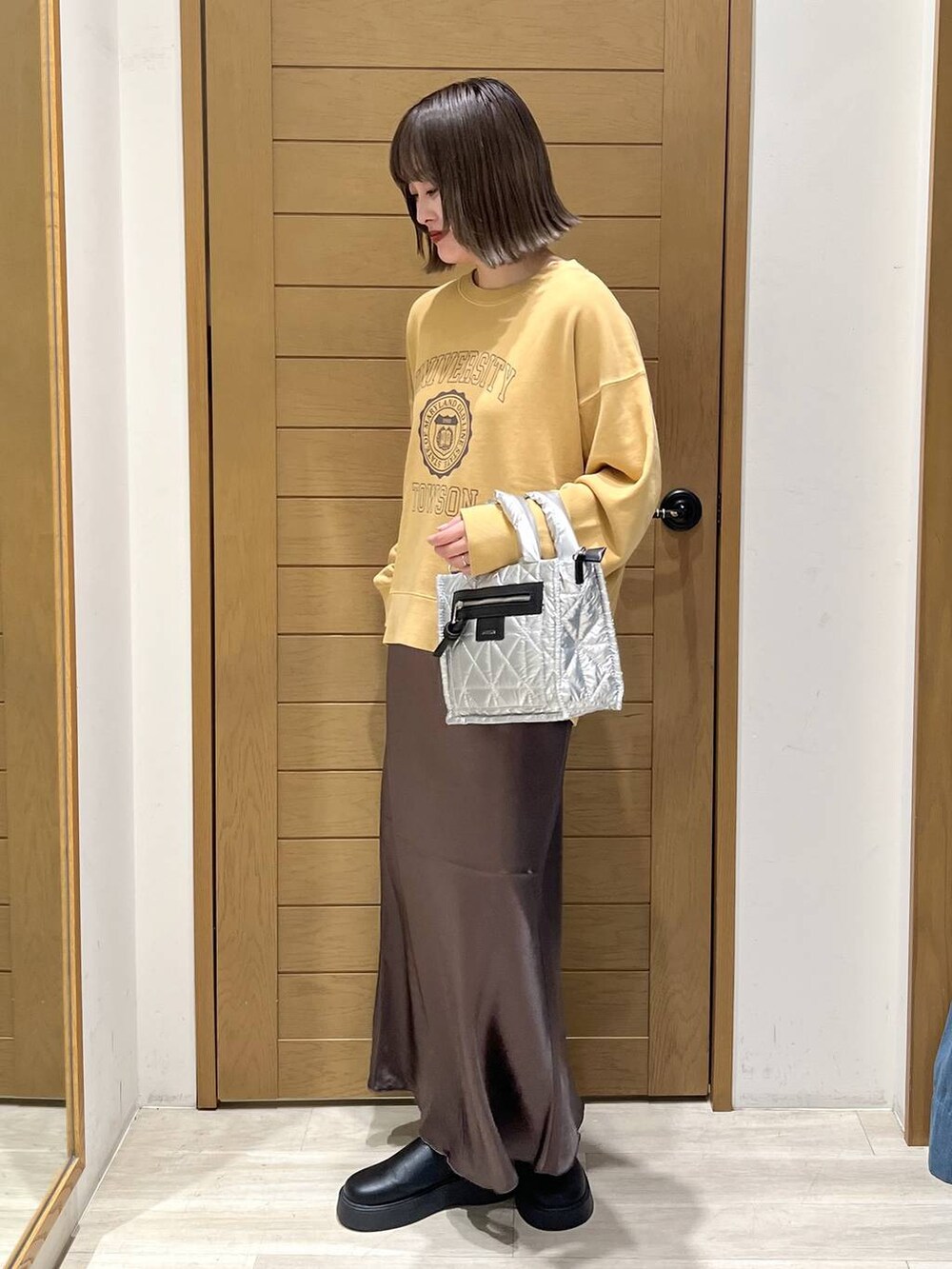 シルバー系のショルダーバッグ、ブラック系のサンダル、イエロー系のスウェットを着用したレディースの秋コーディネートの3枚目の写真