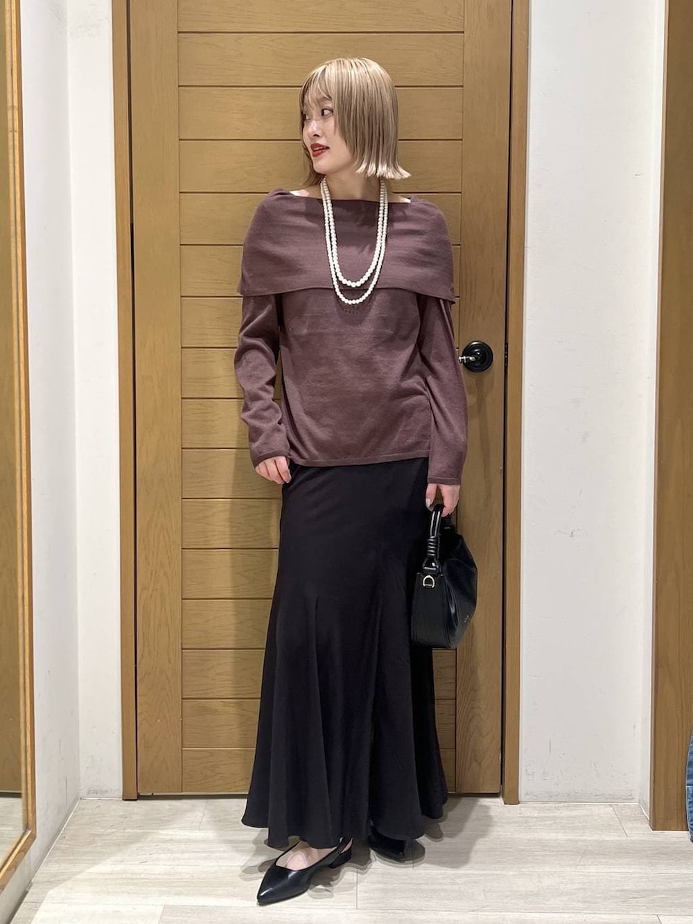 ブラック系のハンドバッグ、ブラック系のパンプス、ブラウン系のニット/セーターを着用したレディースの春コーディネートの2枚目の写真